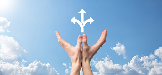 Male hand holding icon with three directions icon on blue background. Doubt, having to choose between three different choices indicated by arrows pointing in opposite direction concept. Ways