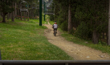 Two People Riding Bicycles On A Path Through The Forest And Under The Ski Lifts Of A Ski Resort