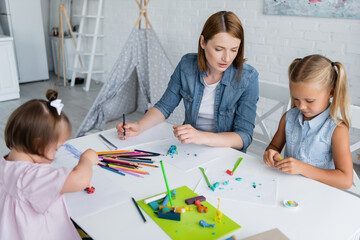 blurred and disabled kid holding pencil with plasticine near teacher and girl in kindergarten