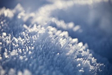 White ice crystals in bright sunlight. Macro photography of ice crystal texture. Snow crystals close-up on a bright frosty winter day. White sparkling snow surface close up. Abstract snowy pattern.