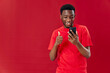 © SHOTPRIME STUDIO - pretty man of African appearance on a red background and touchscreen phone Copy Space