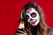 mexican young woman in a costume of Calavera Catrina over red studio background