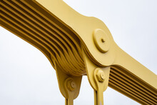 Close Up Detail View Of A Suspension Bridge Joint, Metal Plates Painted Yellow Isolated Against A White Sky, Horizontal Aspect
