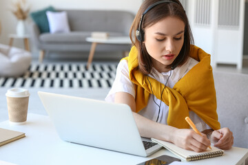 Wall Mural - Young woman with laptop writing something in notebook at home