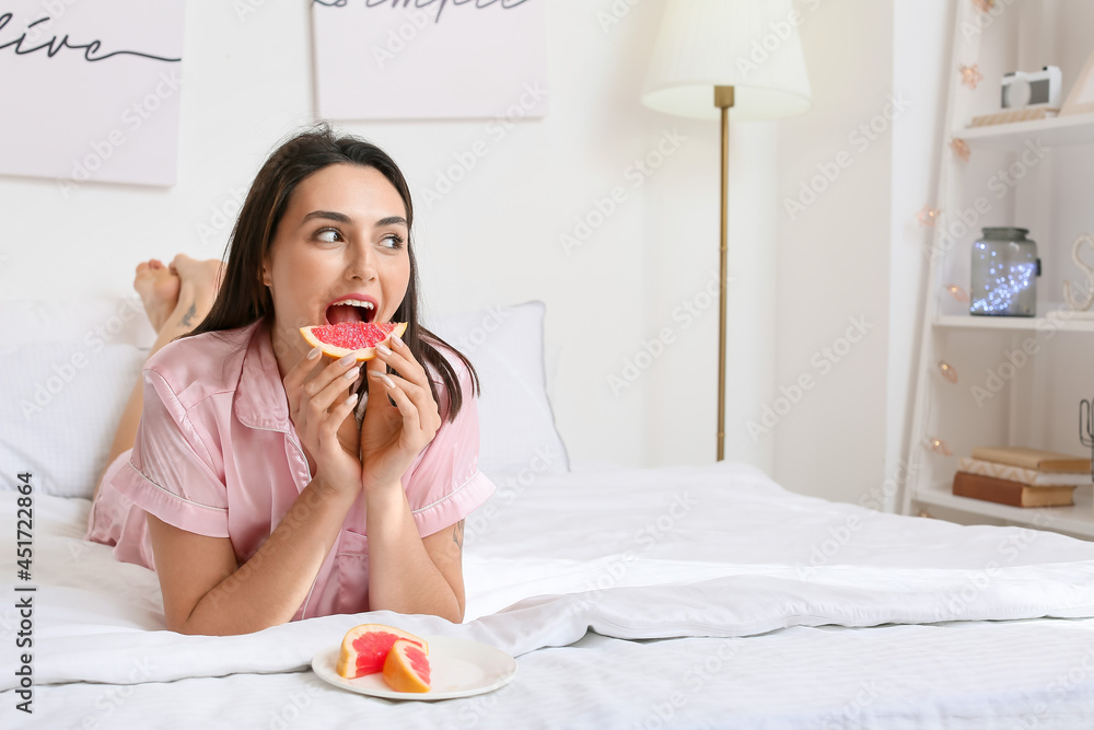 Young woman eating grapefruit in bedroom