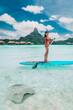 © Maridav - SUP Stand-up paddle board woman wwimming with stingrays tourist tour activity happy Asian woman on Bora Bora island beach at Tahiti overwater bungalow hotel, holiday travel vacation.