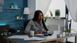 © DC Studio - Black student drinking coffee while searching business information on internet using computer working at communication project. Focused woman sitting at desk in living room analyzing homework graphic
