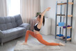 Young woman is practicing warrior pose I virabhadasana doing yoga at home. Sport fitness training stretching workout yoga wellness concept. Concentration flexibility energy concept, standing asana.