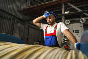 Poster - A young factory workman rolls heavy coil of electric cable