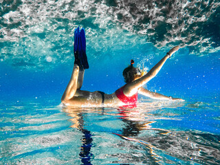 Wall Mural - Free diver woman with white fins glides underwater with amazing sun rays. Freediving underwater in ocean