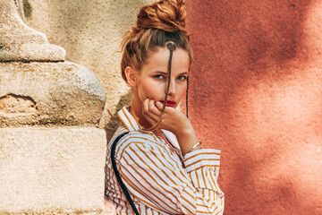 Poster - Outdoor portrait of a attractive young woman looking at the camera on a sunny day against a red wall. Young female student posing in the city street.