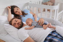 Tired Young Parents With Their Baby Sleeping In Bed At Home