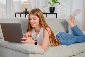 Wall Mural - beautiful young woman with laptop at home on the couch. chatting online, lifestyle