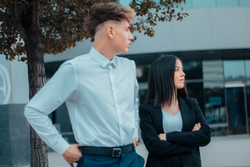 Hombre y chica joven de pie y mirando serios en su descanso de trabajo empresarial junto al edificio con cristaleras