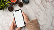 © bongkarn - female hands in sweater holding blank screen smartphone with copy space on marble background