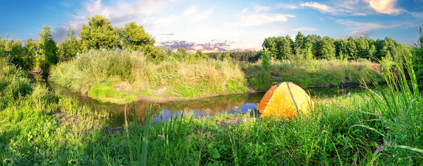 Wall Mural - orange tent on river bank covered with green lush grass