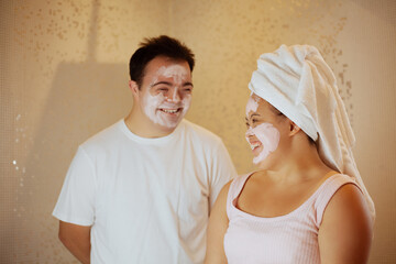 Young biracial couple with Down Syndrome with face masks having fun in the bathroom