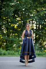 Wall Mural - Young lady wearing an elegant dark blue dress is standing in the middle of the road in the park