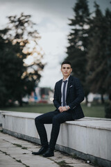 Poster - Young Bosnian male wearing a stylish suit is posing sitting in the park