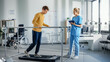 © Gorodenkoff - Hospital Physical Therapy Room: Patient with Injury Walking on Treadmill Holding for Parallel Bars, Professional Physiotherapist Assists, Helps, Trains Disabled Person Do Rehabilitative Physiotherapy