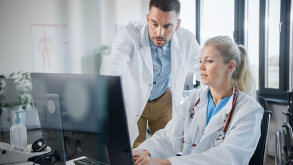 Wall Mural - Hospital Medical Doctor's Office: Two Professional Physicians Talking, Solving Problem, Working on Computer. Specialists Discuss Patient Online Treatment, Writing Digital Medicine Prescriptions