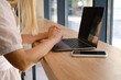 © Iuliia Pilipeichenko - The girl sits at a table in front of a laptop and uses a smartphone for work. Remote work from home. Office desk with laptop and smartphone. Business background. Home office