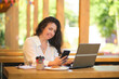 © yavdat - Portrait of beautiful senior businesswoman sitting at cafe with laptop looking away and thinking. Mature woman at coffee shop. laughing happily indoors.