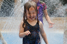 Little Girl Happily Playing And Laughing Under Fountains At A Water Park