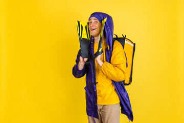 Wall Mural - Comic portrait of young man, delivery guy in uniform isolated on yellow studio background. Concept of humor, safety, service. Complementary colors