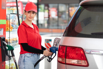 Wall Mural - woman worker holding petrol hose and refueling vehicle or car at gas station