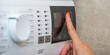 © SERSOLL - Washing machine. The hand turns on the washing machine or the choice of the washing program. Washing clothes. Banner for website or print with copy space