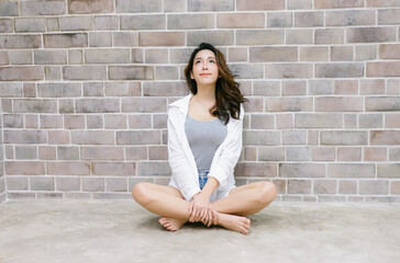 Portrait of young Korean woman sitting on the floor and looking up at the brick wall Background. Beautiful Asian woman healthy and beauty lifestyle girl Concept.