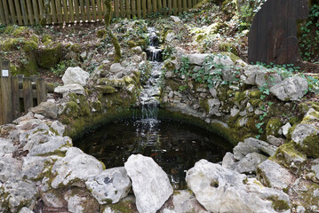 Poster - Closeup view of the water flowing into the circular place made out of stones covered in moss