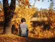 © pavelkant - A young man is sitting by a tree and listening to music with headphones. Rear view. Autumn mood concept