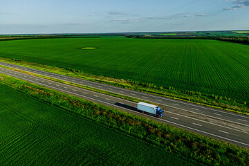 Wall Mural - one blue truck  on the higthway at sunset among the green fields with goods cargo delivery. seen from the air. Aerial view landscape. drone photography.