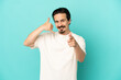 © luismolinero - Young caucasian man isolated on blue background making phone gesture and pointing front