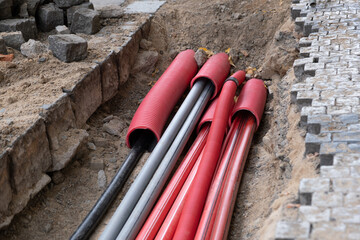 Wall Mural - A large number of electric and high-speed Internet Network cables in red corrugated pipe are buried underground on the street covered with cobblestones. 