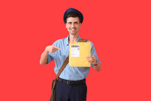 Handsome Young Postman Pointing At Letter On Color Background