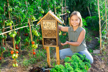 Little girl sitting beside insect hotel in kitchen garden.