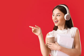 Canvas Print - Young woman with book, cup of coffee and headphones showing something on color background