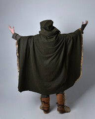 Full length  portrait of  young handsome man  wearing  medieval Celtic adventurer costume with hooded cloak facing away,  isolated on studio background.