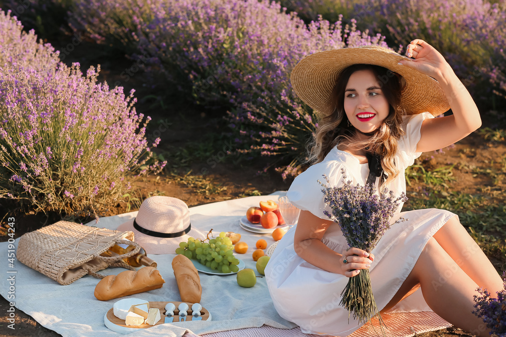 Beautiful young woman having picnic in lavender field