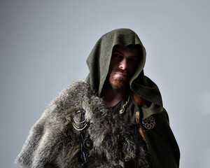Close up  portrait of  young handsome man  wearing  medieval Celtic adventurer costume with hooded fur cloak,  isolated on studio background.