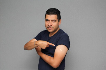 Happy Latino adult man shows his arm that just received the Covid-19 vaccine in the new normal for the coronavirus pandemic
