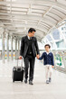 © suphaporn - a business man wearing a suit with a suitcase He took his lovely son's hand. and walk together along the corridor of the sky train  he smiled happily to his son - happy family Dad and son concept