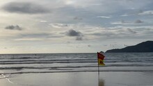 Tropical Beach, Sea, Waves, Tourists Resting. Water Scooter, Jet Ski Moving Along The Surface Of The Water. Red Yellow Lifeguard Flag Allows People From Swimming. Cloudy Sky. Sunset. Thailand. Phuket 