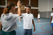 Happy African American schoolboy gives high-five to physical education teacher at school gym.