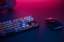 Computer Keyboard With Colorful Backlit, Mouse And Headphones Laying On Desk. Purple Light From Top.