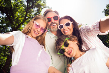 Wall Mural - Photo of funny shiny family wear casual clothes dark glasses smiling recording video outdoors urban city park