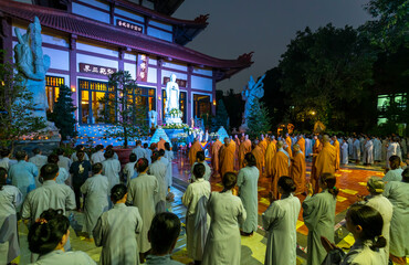 Monks and Buddhists are reverently bowing to Buddha during evening ceremony for Amitabha Buddha at an ancient temple in Ho Chi Minh City, Vietnam